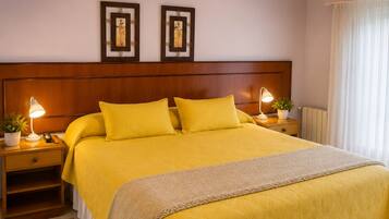 A large bed with a wooden headboard, two bedside tables with lamps, a woven rug, and a window with curtains.