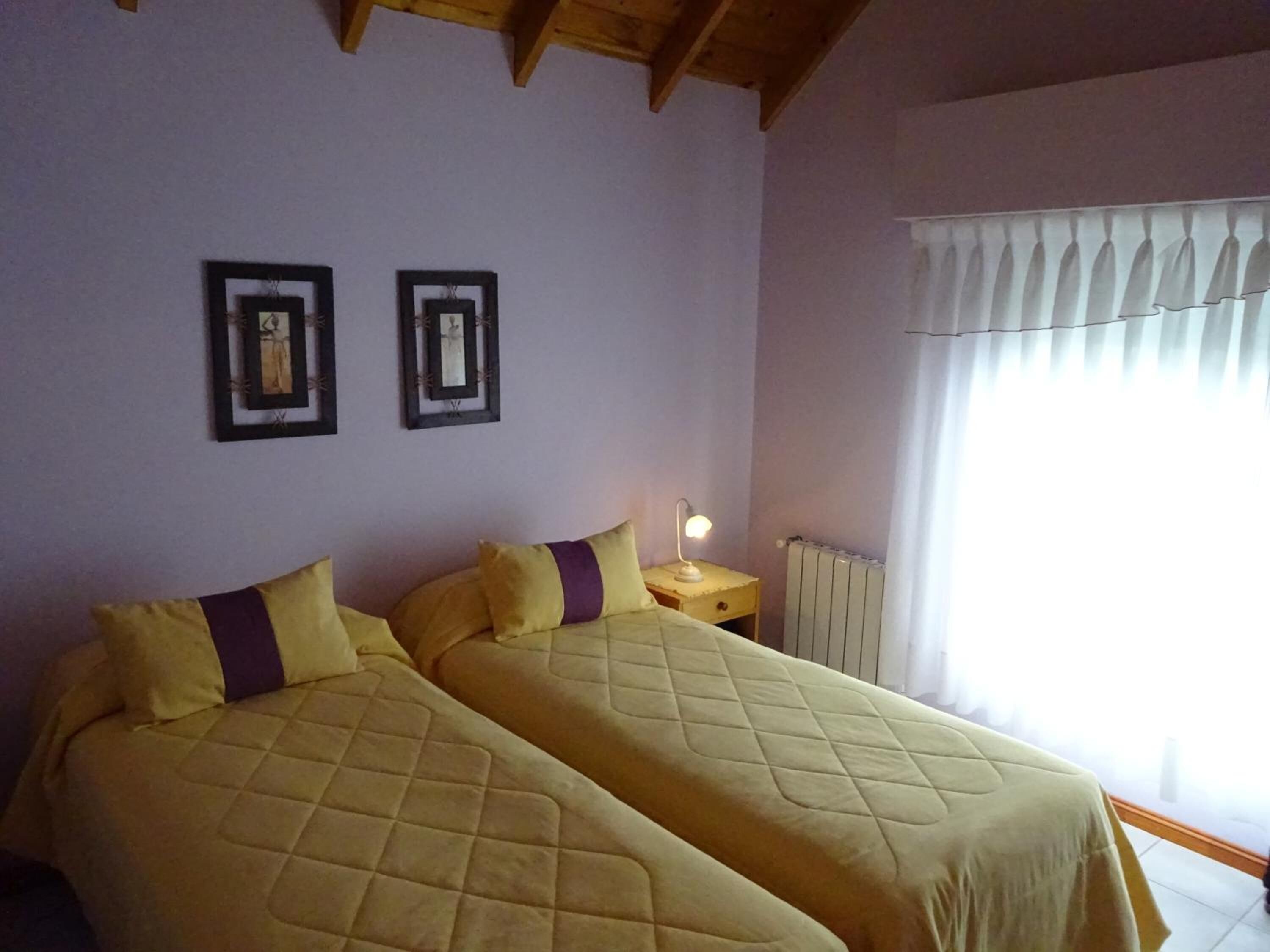 Una habitación con dos camas, una mesita de noche con lámpara, un radiador y una ventana con cortinas.