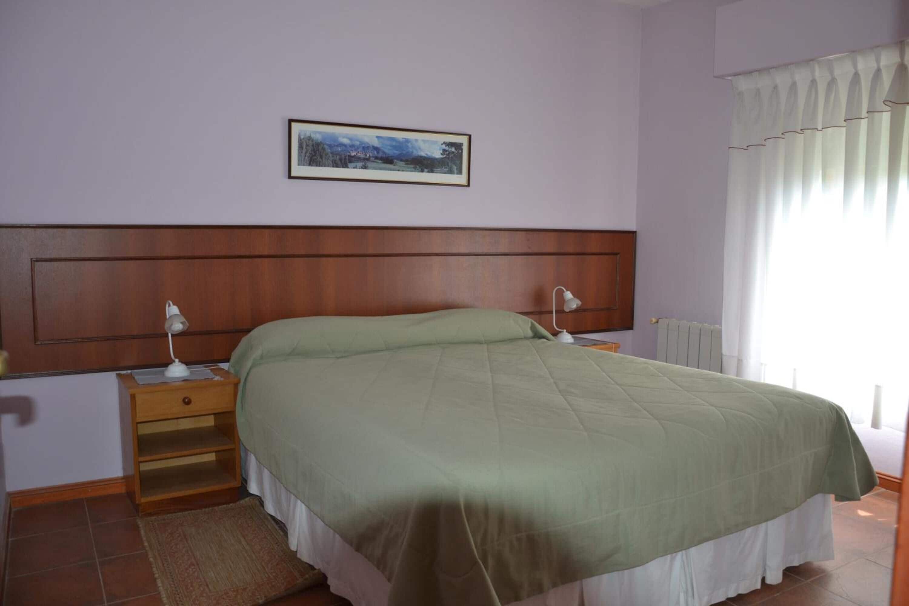 Une chambre à coucher avec une tête de lit en bois, une couvre-lit verte, une table de chevet avec une lampe et un tableau encadré au mur.