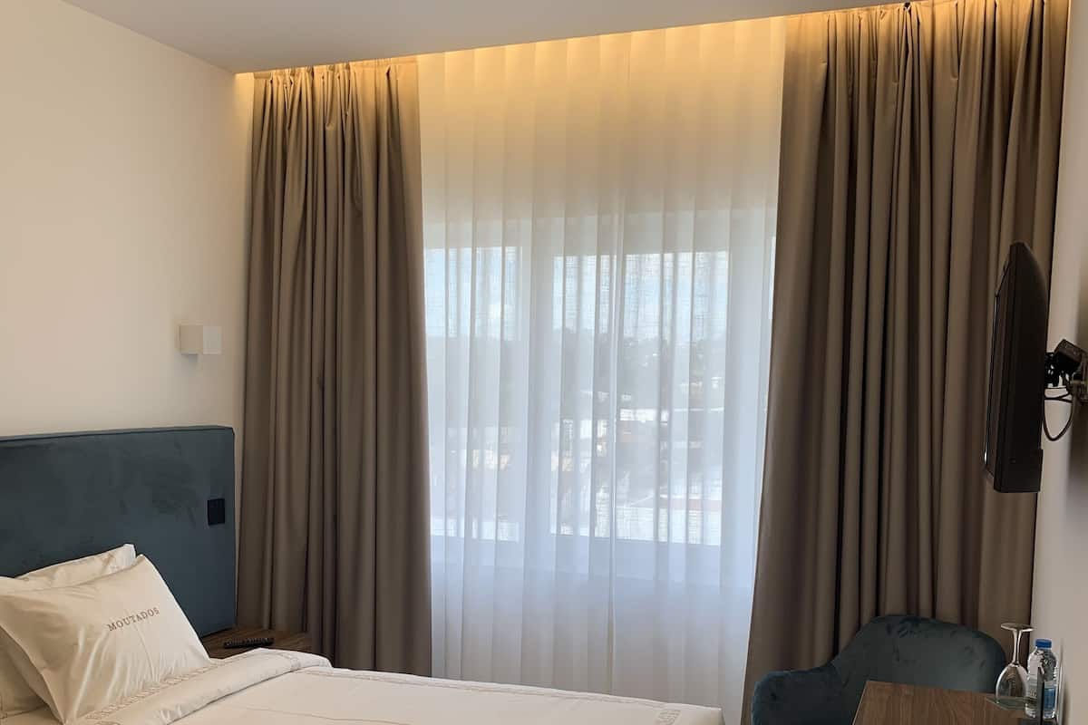 A hotel room with a bed, a desk, a chair, and a window with curtains.
