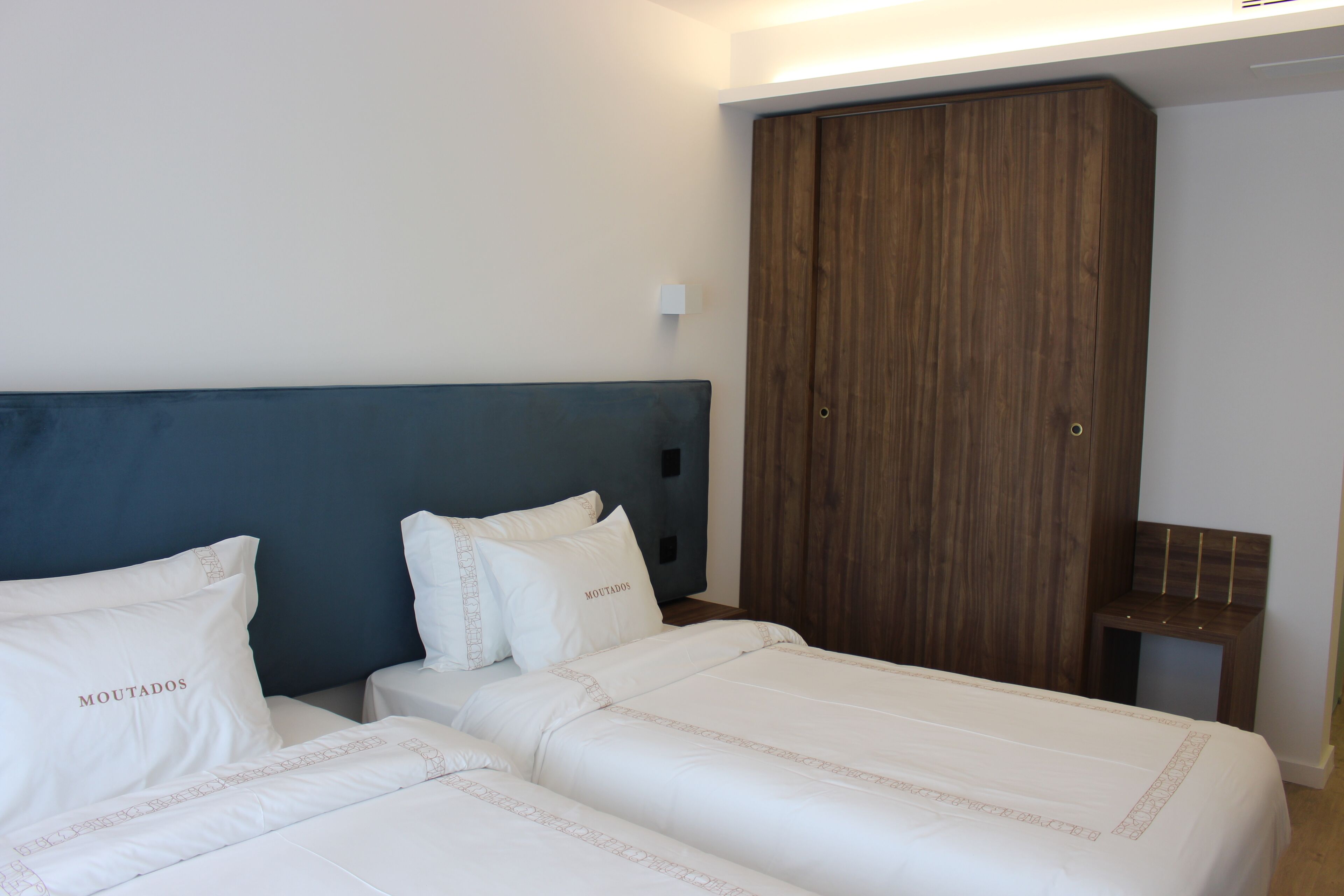 Une chambre avec deux lits, une tête de lit bleu foncé et une armoire en bois.