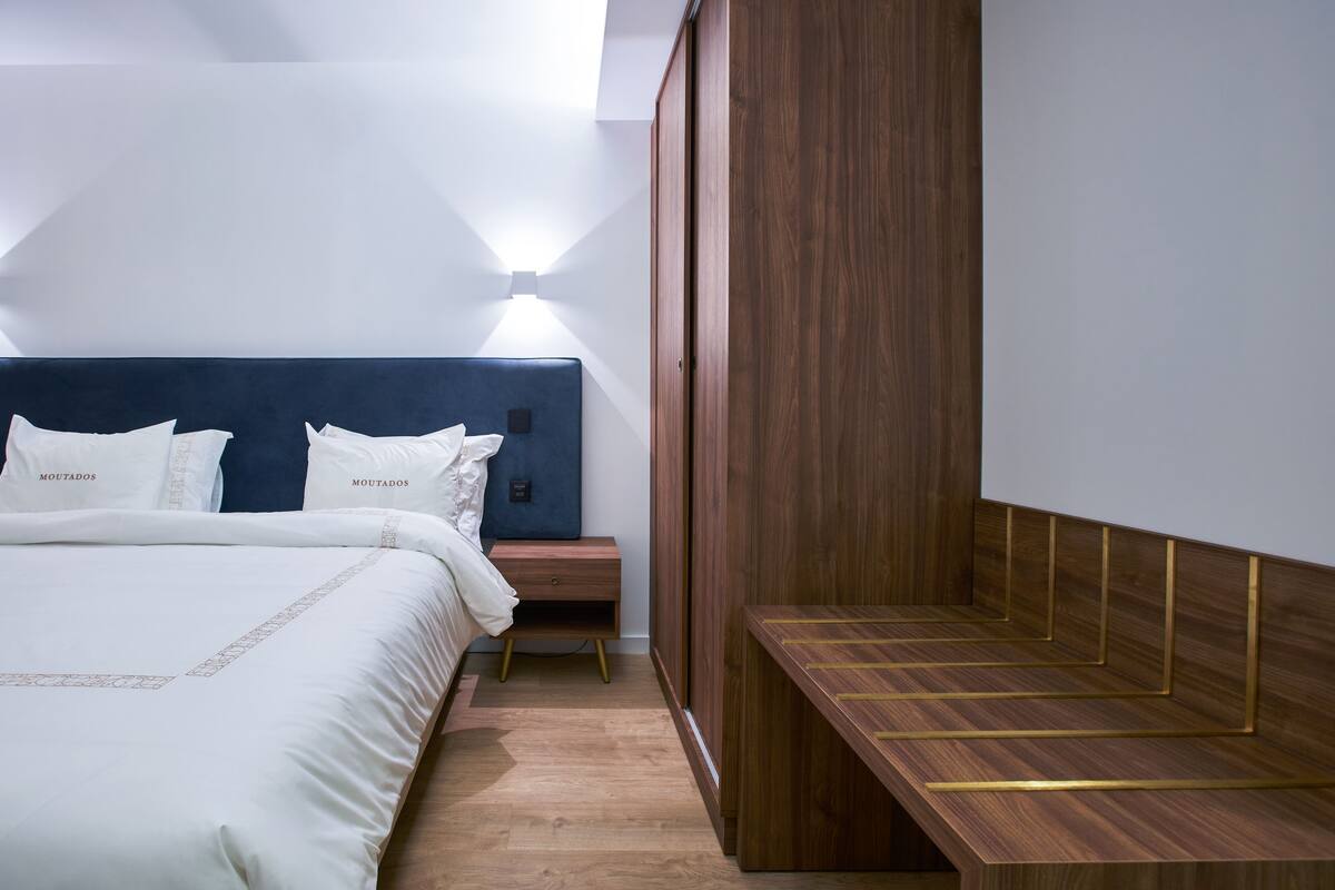 A modern hotel room with a large bed, a wooden nightstand, and a built-in bench.