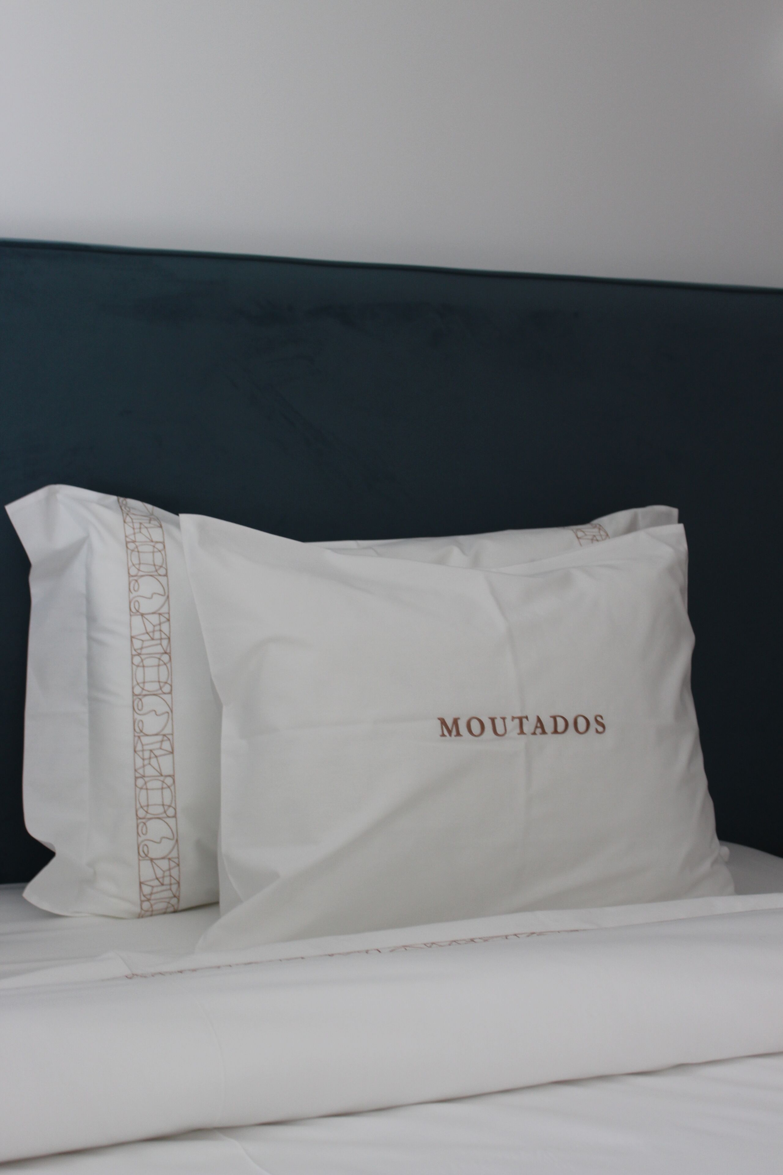 En seng med hvide sengetøj og puder, hvoraf den ene har 'MOUTADOS' broderet på.