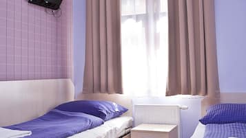 A hotel room with two beds, a flat-screen TV mounted on the wall, a window with curtains, and a wooden floor.