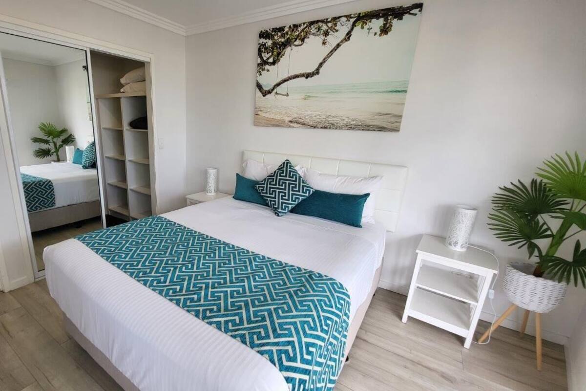 A bedroom with a bed, a wardrobe, a nightstand, and a potted plant.