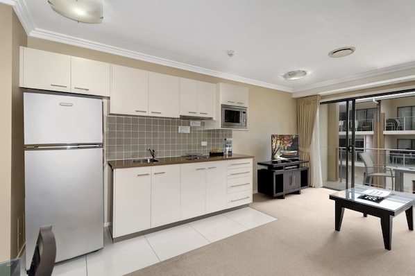 Una cocina moderna con armarios blancos, un refrigerador de acero inoxidable y un microondas. Hay un comedor con una mesa de vidrio y sillas.