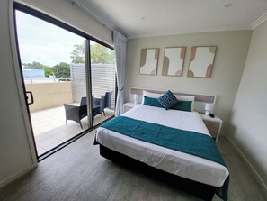 Ein modernes Hotelzimmer mit einem großen Bett, einer Schiebetür zum Balkon und Blick ins Freie.