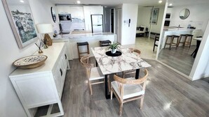 Una cocina moderna con armarios blancos, una isla de mármol y un comedor con mesa y sillas.
