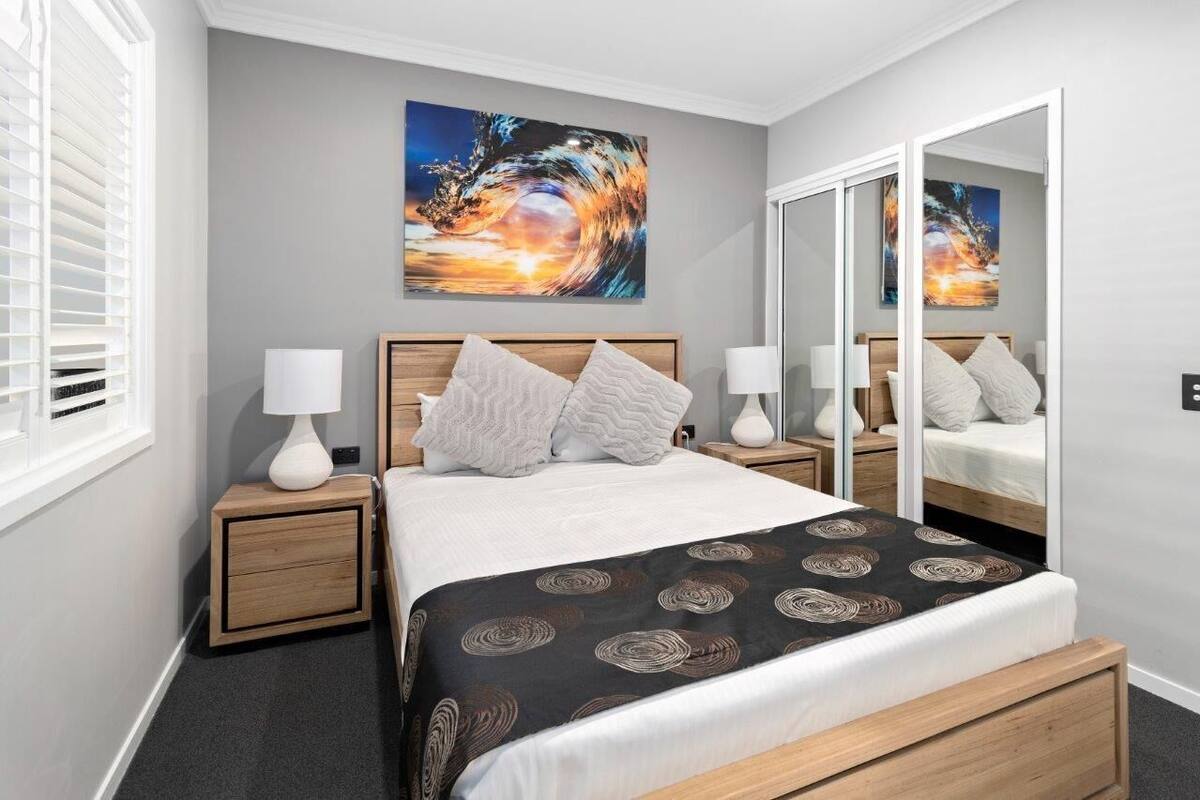 A modern bedroom with a bed, two nightstands, a mirror, and a large abstract painting on the wall.