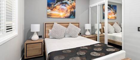 Une chambre à coucher moderne, avec un lit, deux tables de chevet, un miroir et un grand tableau abstrait accroché au mur.