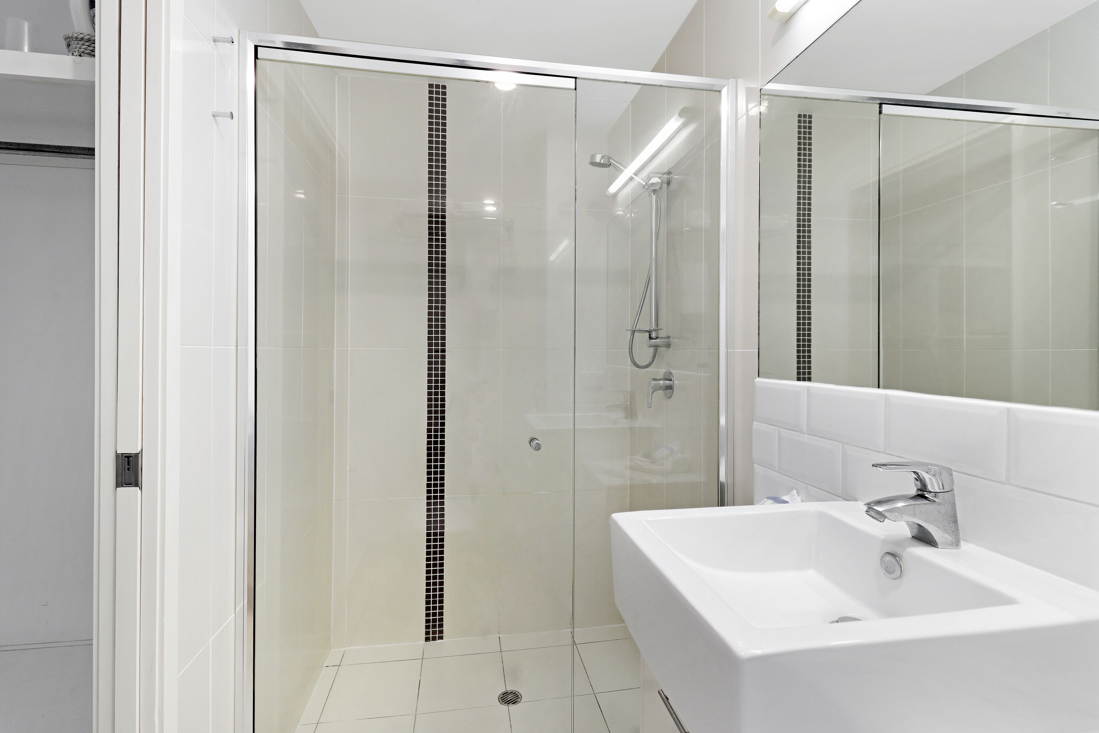 Un baño moderno con ducha envuelta en vidrio, un lavabo blanco y un espejo grande.