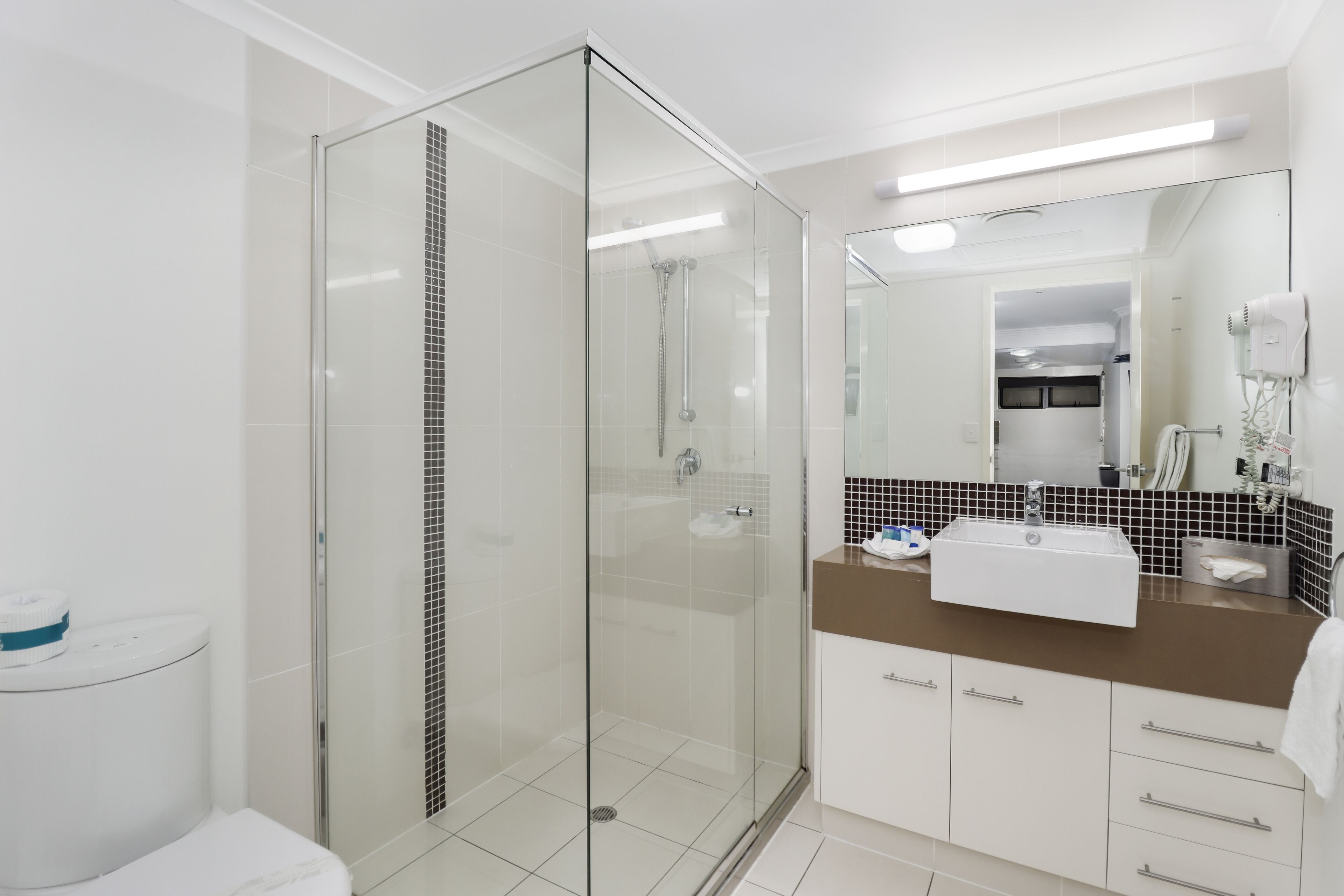 Un baño moderno con ducha de vidrio, inodoro blanco, lavamanos con encimera marrón y espejo sobre el lavamanos.