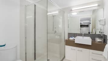 Un baño moderno con ducha de vidrio, inodoro blanco, lavamanos con encimera marrón y espejo sobre el lavamanos.