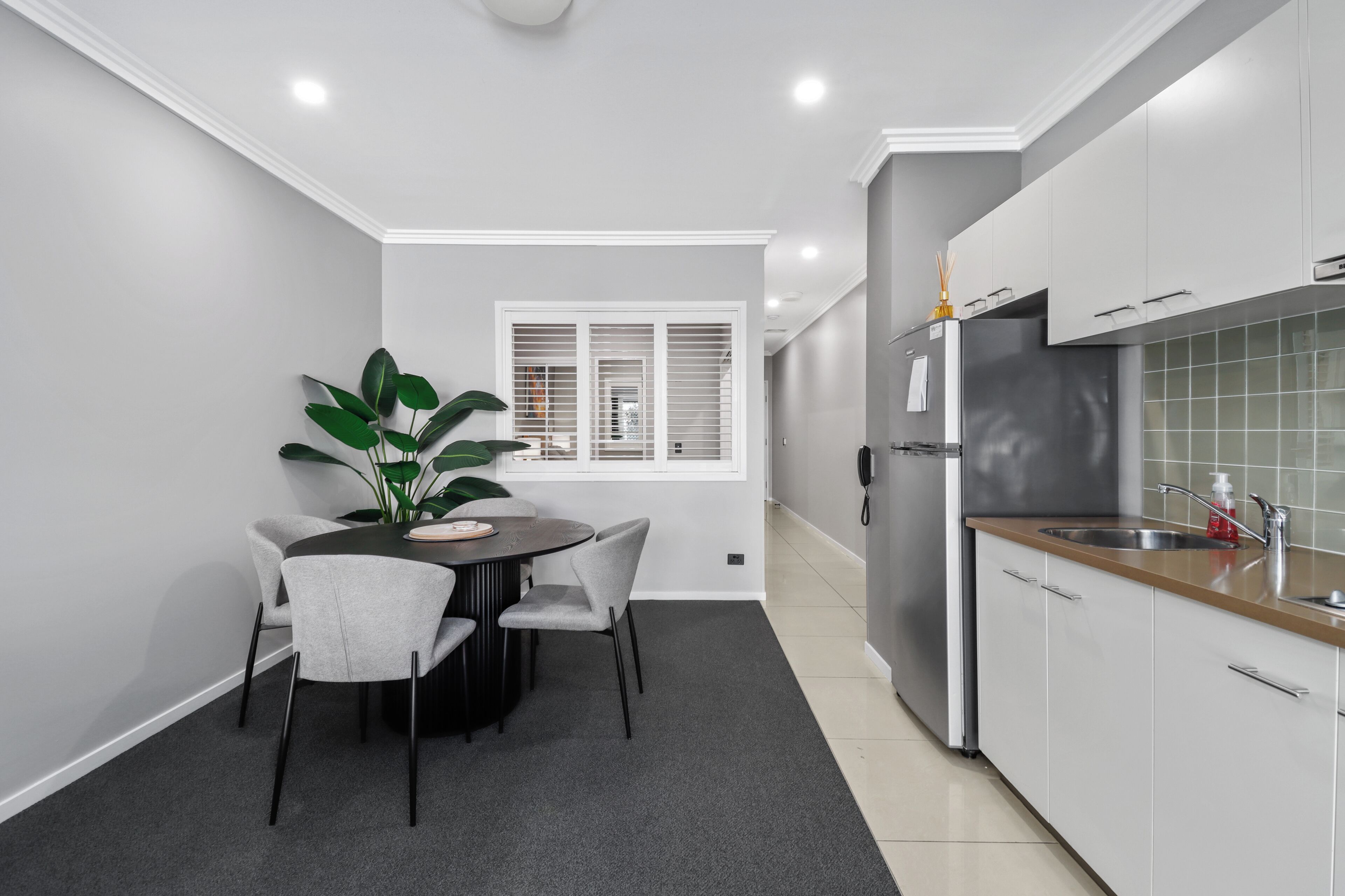 A compact kitchen with a dining area, featuring a round table, chairs, a potted plant, and modern cabinetry.