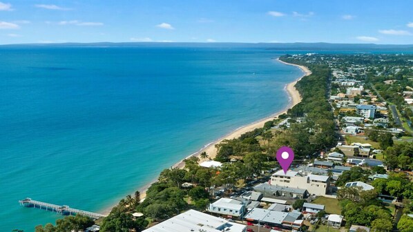 Ein Luftbild einer Küstenregion mit Strand, Wohnhäusern und einem Steg, der sich ins Wasser erstreckt.