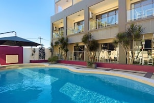 Un hotel moderno con piscina, zona de estar al aire libre y un edificio de varios pisos con balcones.
