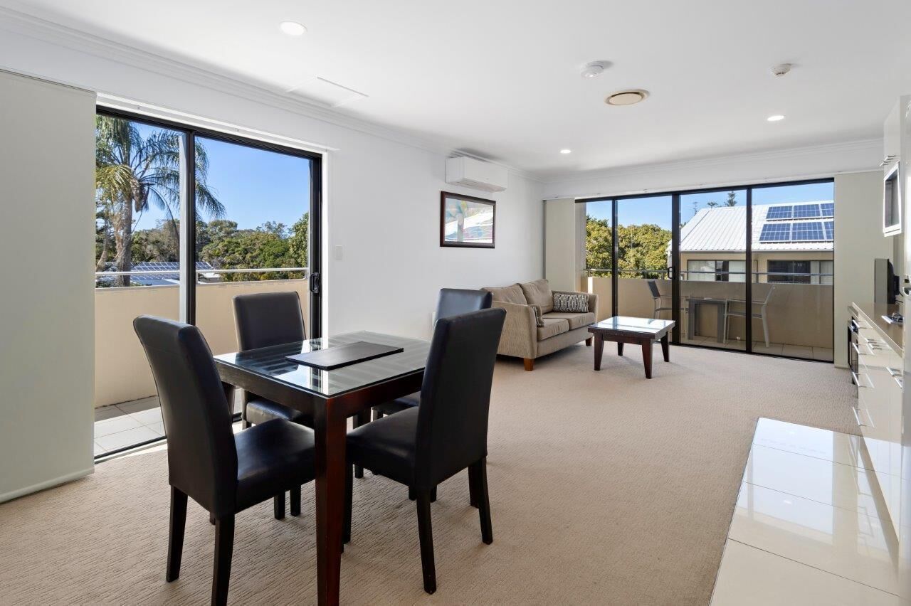 A modern living room with a glass dining table, two chairs, a sofa, and a coffee table.