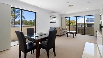 A modern living room with a glass dining table, two chairs, a sofa, and a coffee table.