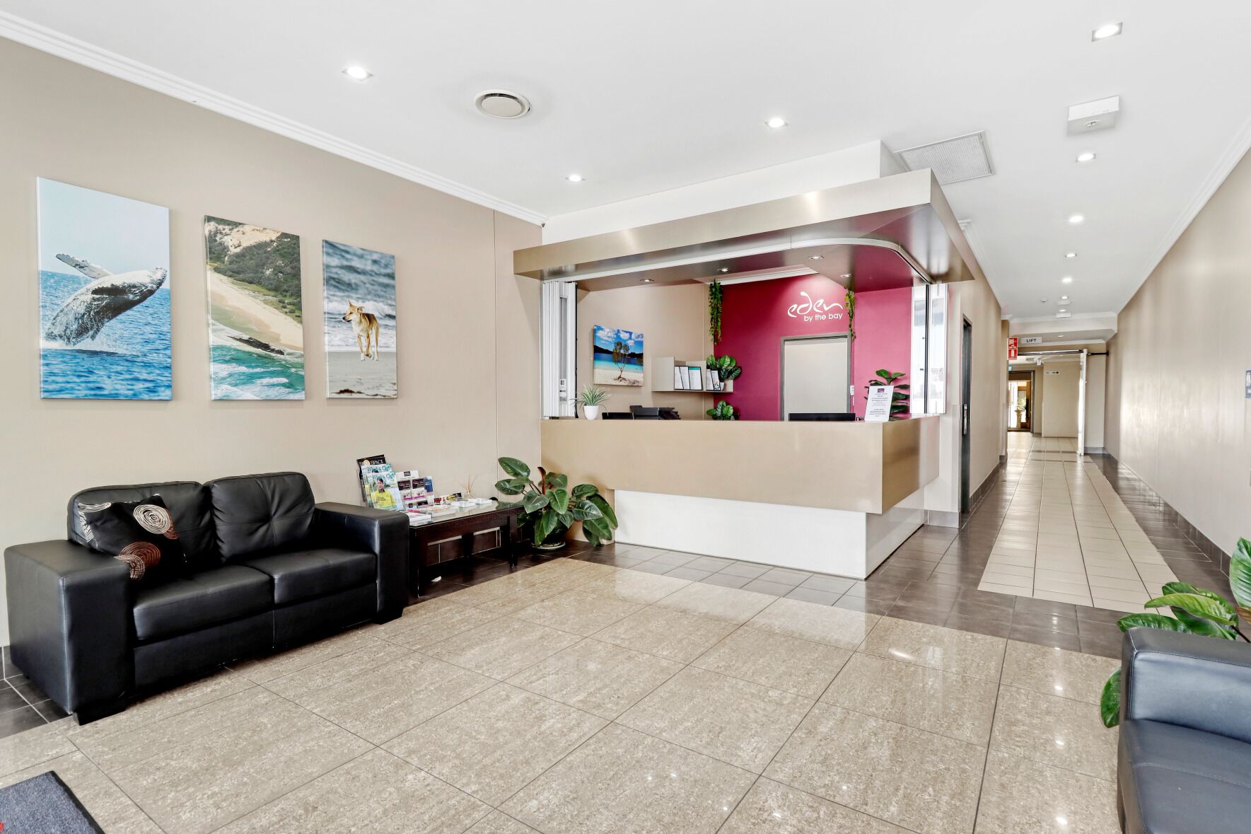 A hotel reception area with a black leather sofa, a reception desk, and two framed pictures on the wall.