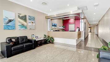 A hotel reception area with a black leather sofa, a reception desk, and two framed pictures on the wall.