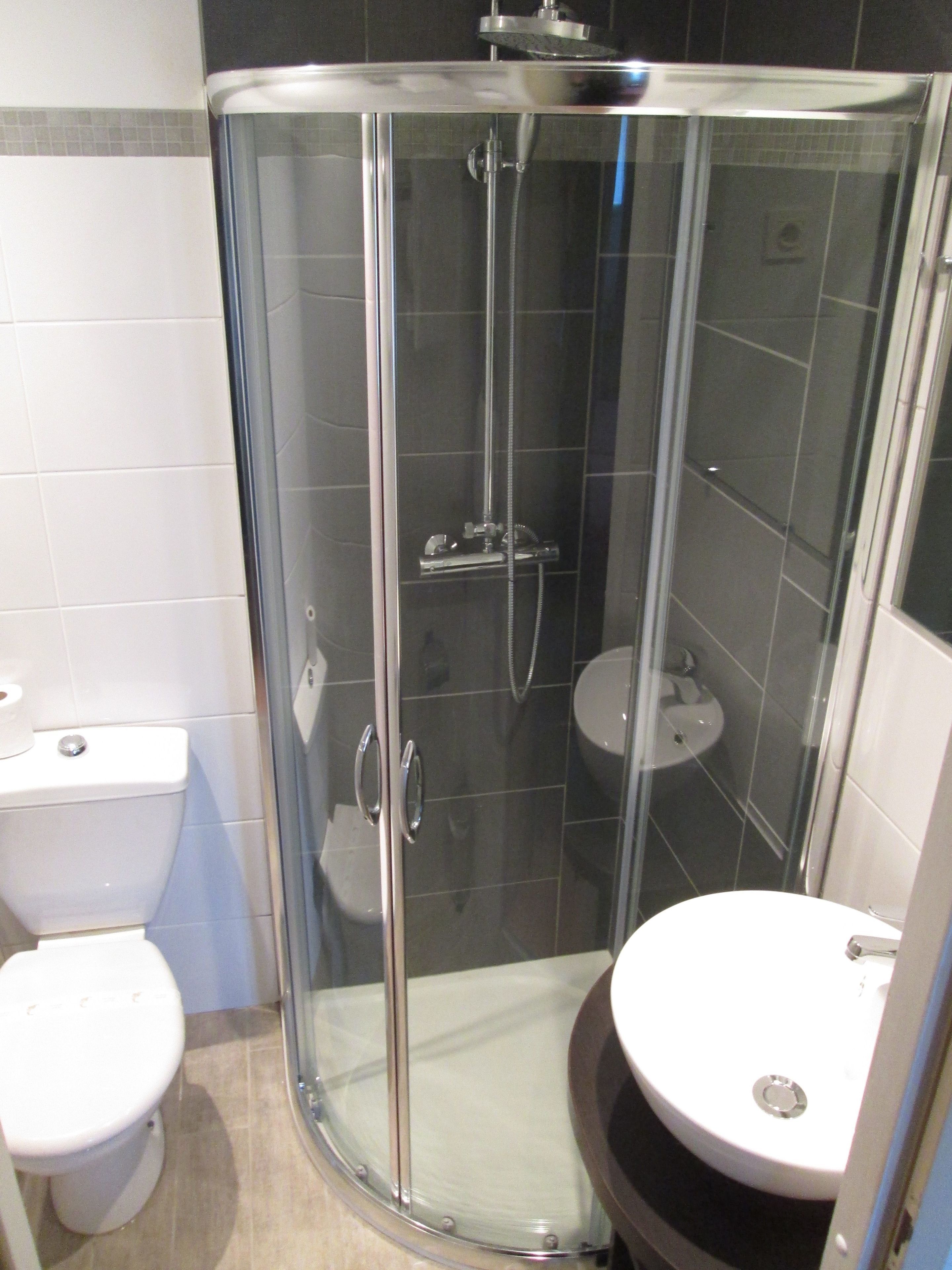 A glass-enclosed shower stall with a handheld showerhead, a toilet, and a sink.
