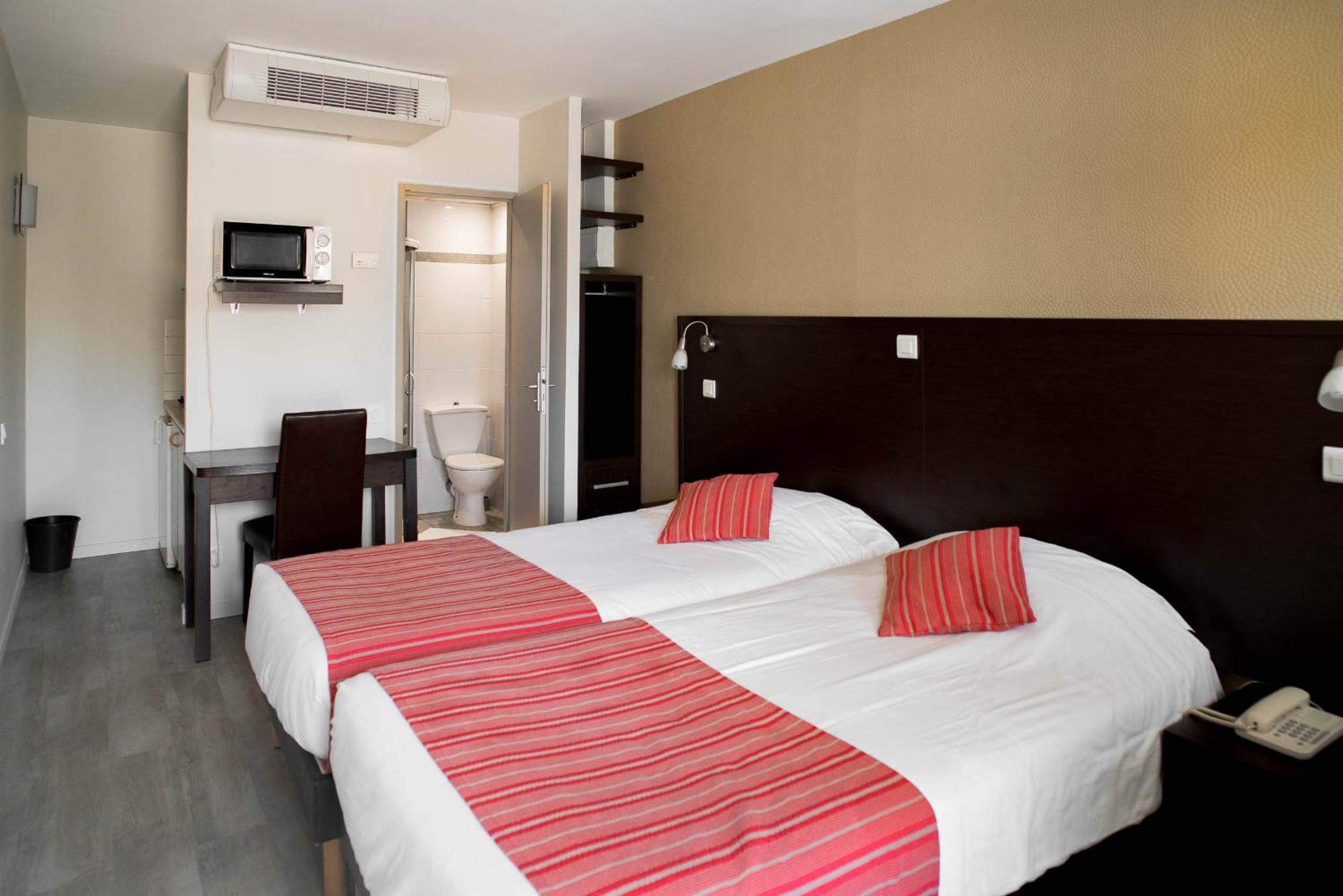 Habitación de hotel con dos camas, un escritorio, una silla, un inodoro y un teléfono.
