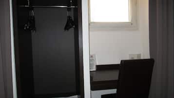 Une pièce avec une armoire en bois sombre, une petite table et une fenêtre avec des stores.