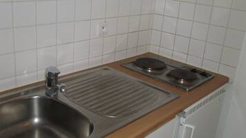 Uma cozinha compacta com uma pia, duas bocas elétricas e um refrigerador pequeno.