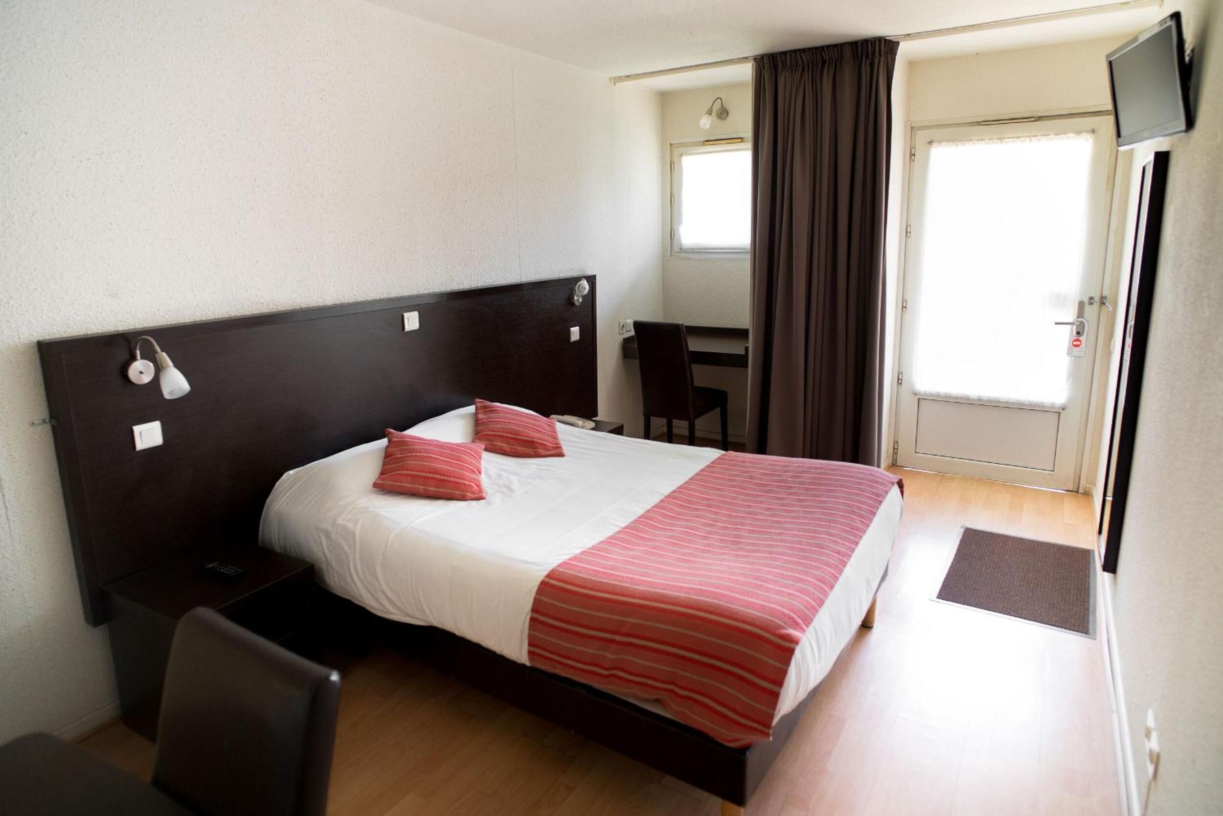 Een hotelkamer met een bed, nachtkastje, stoel, bureau, televisie en gordijnen.
