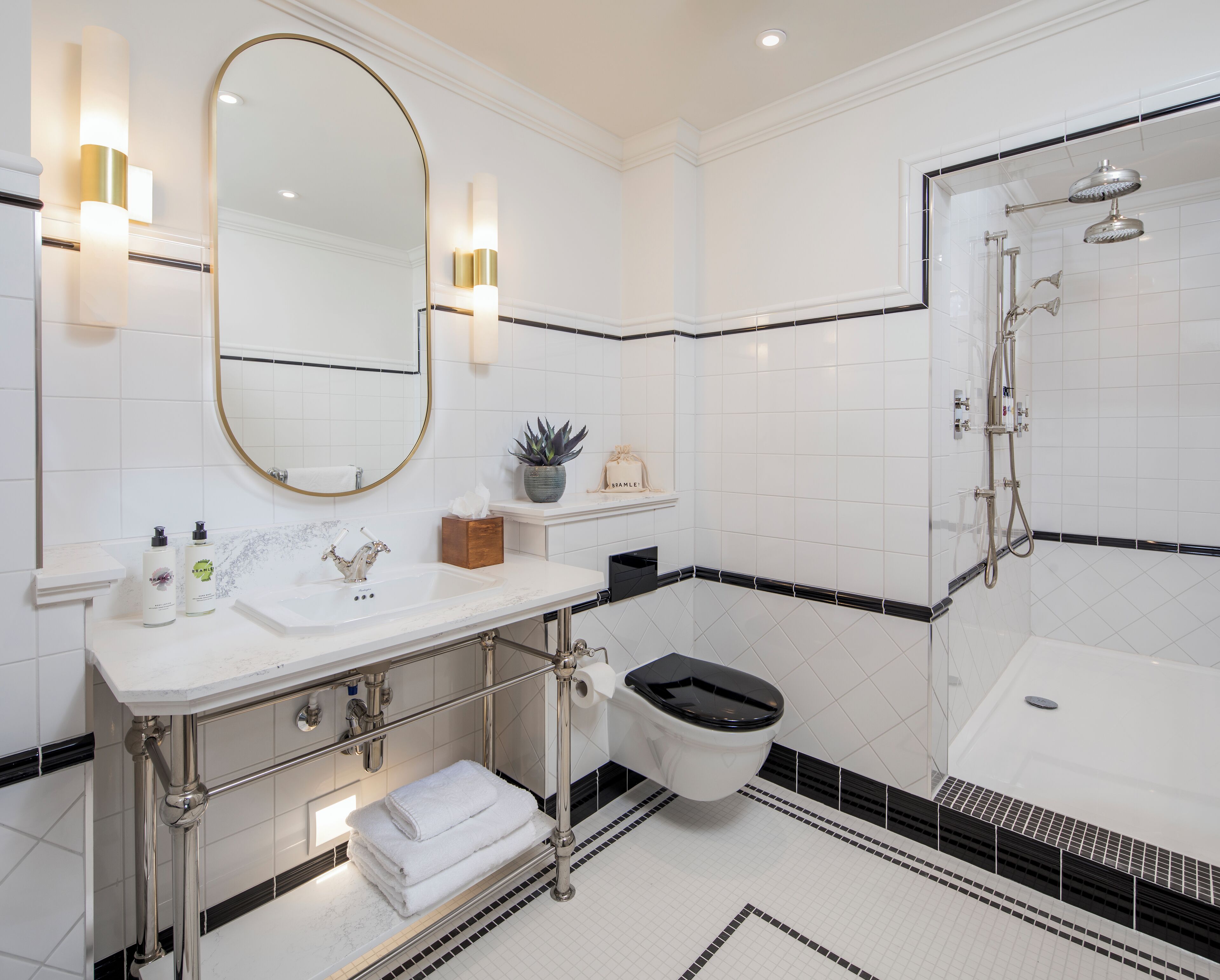 Casa de banho moderna com lavatório branco, espelho e chão em mosaico preto e branco.