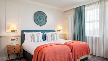 A double bed with white and blue bedding, two red throw blankets, a wall-mounted circular decoration, and a nightstand with a lamp.