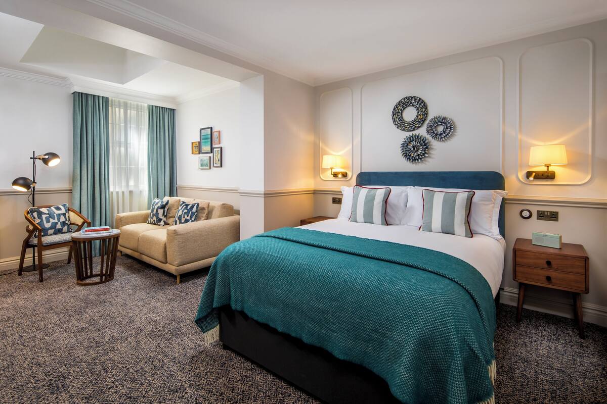 A hotel room with a bed, a chair, a nightstand, and a lamp.