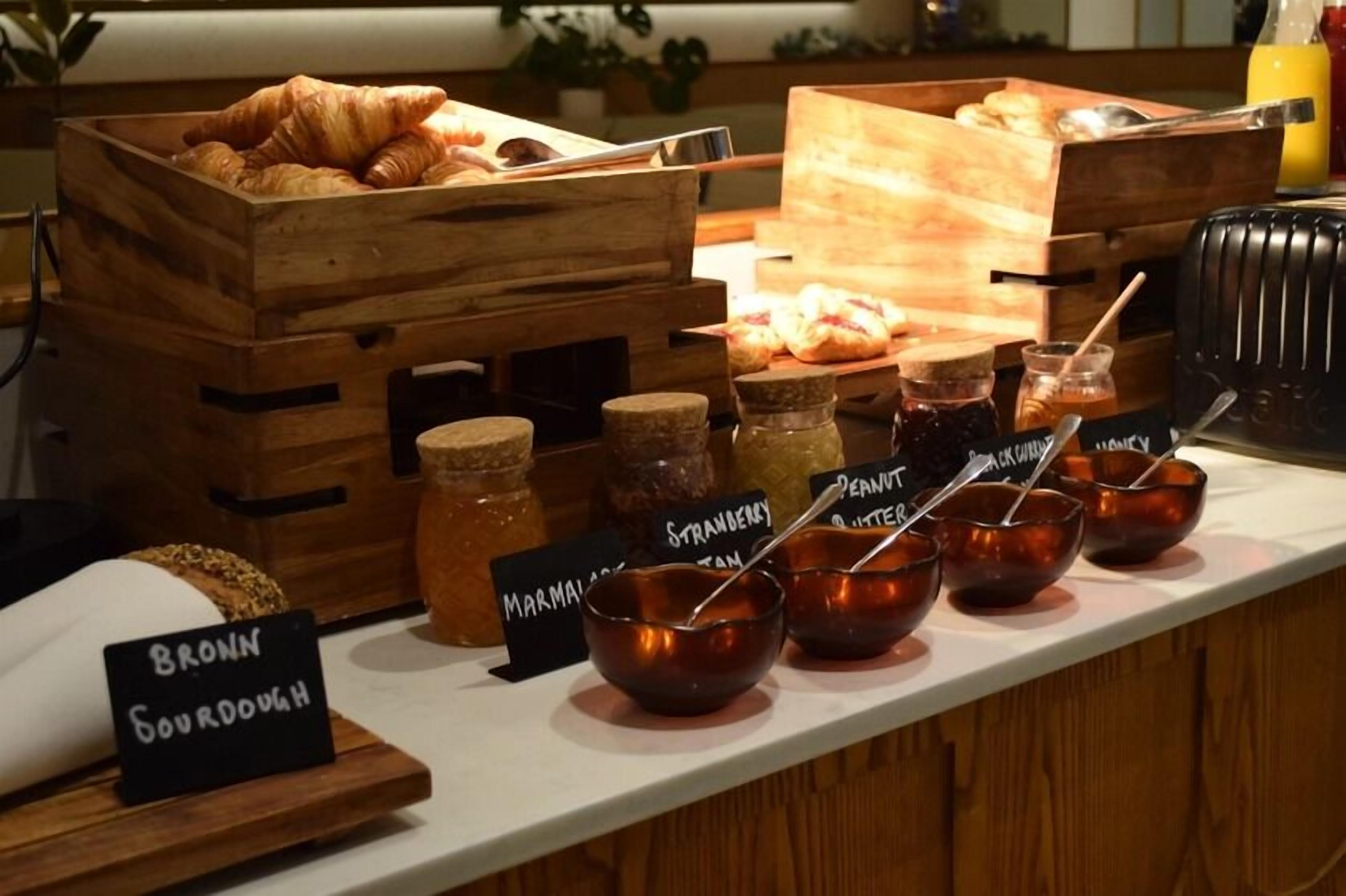 A breakfast buffet with croissants, muffins, and various jams and spreads.
