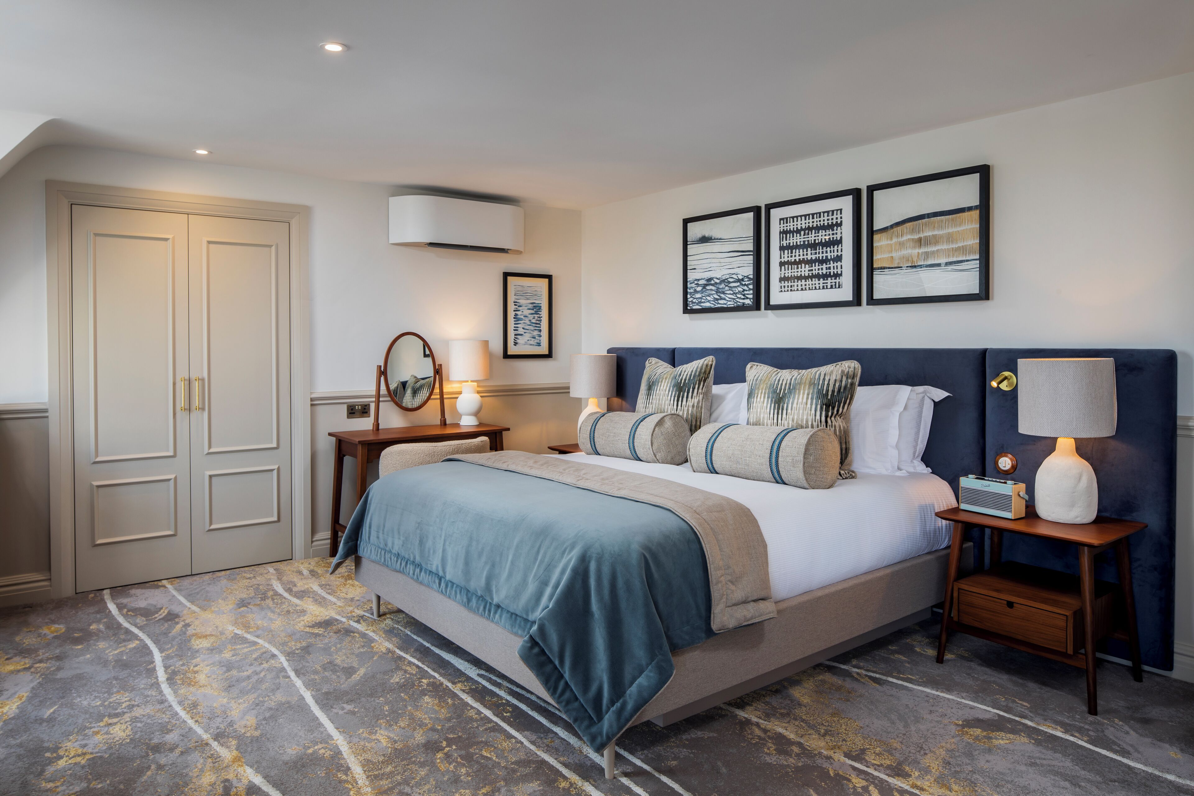 Habitación de hotel con una cama grande, una mesita de noche, un aparador y un aire acondicionado instalado en la pared.