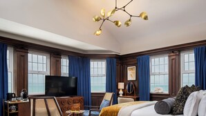 A spacious hotel room with a large bed, a television, a desk with a lamp, and a view of the sea through large windows. - White Horses by Everly Hotels Collection (Brighton)