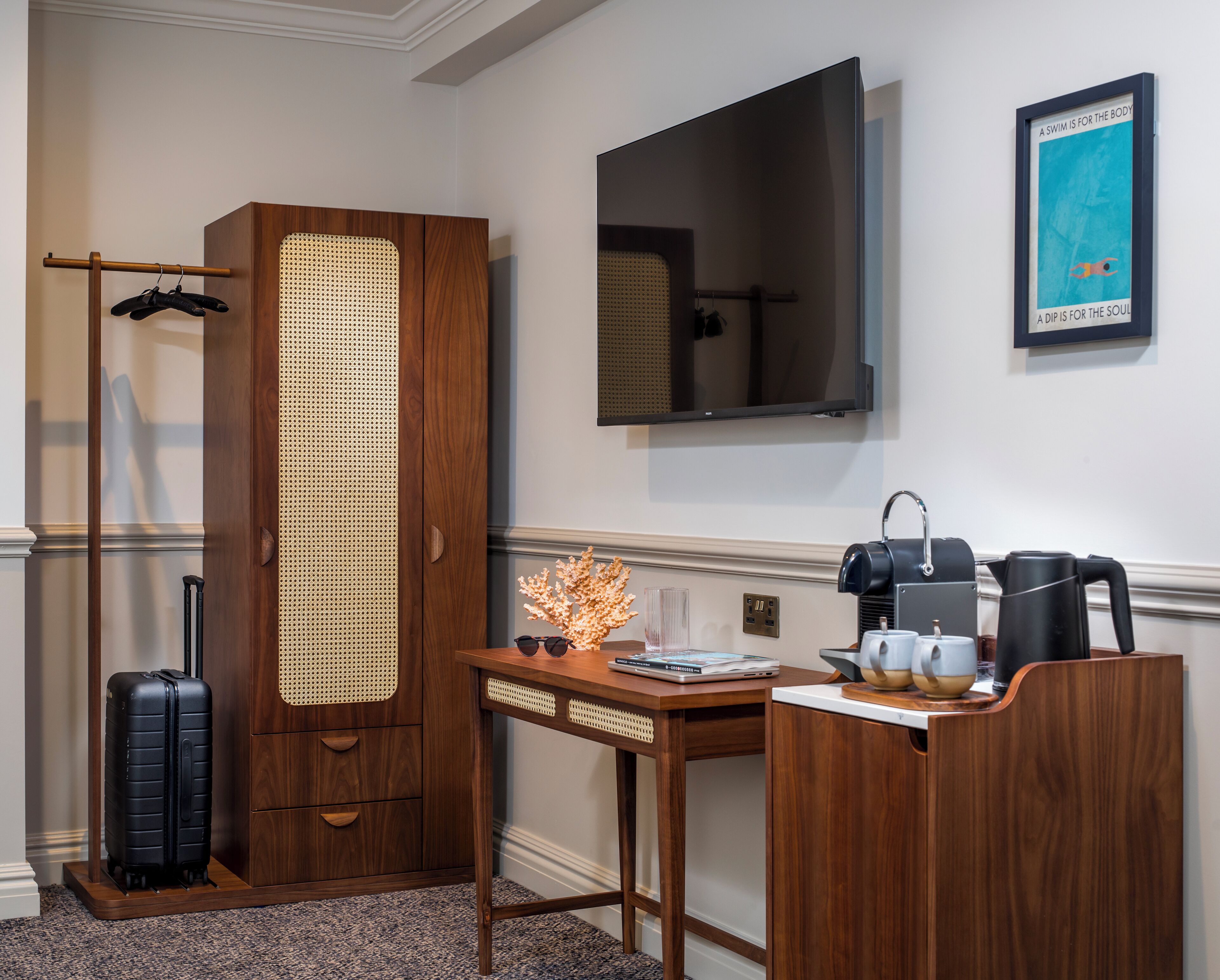 Une chambre d’hôtel avec une armoire en bois, un bureau avec une machine à café, une télévision et une affiche accrochée au mur.