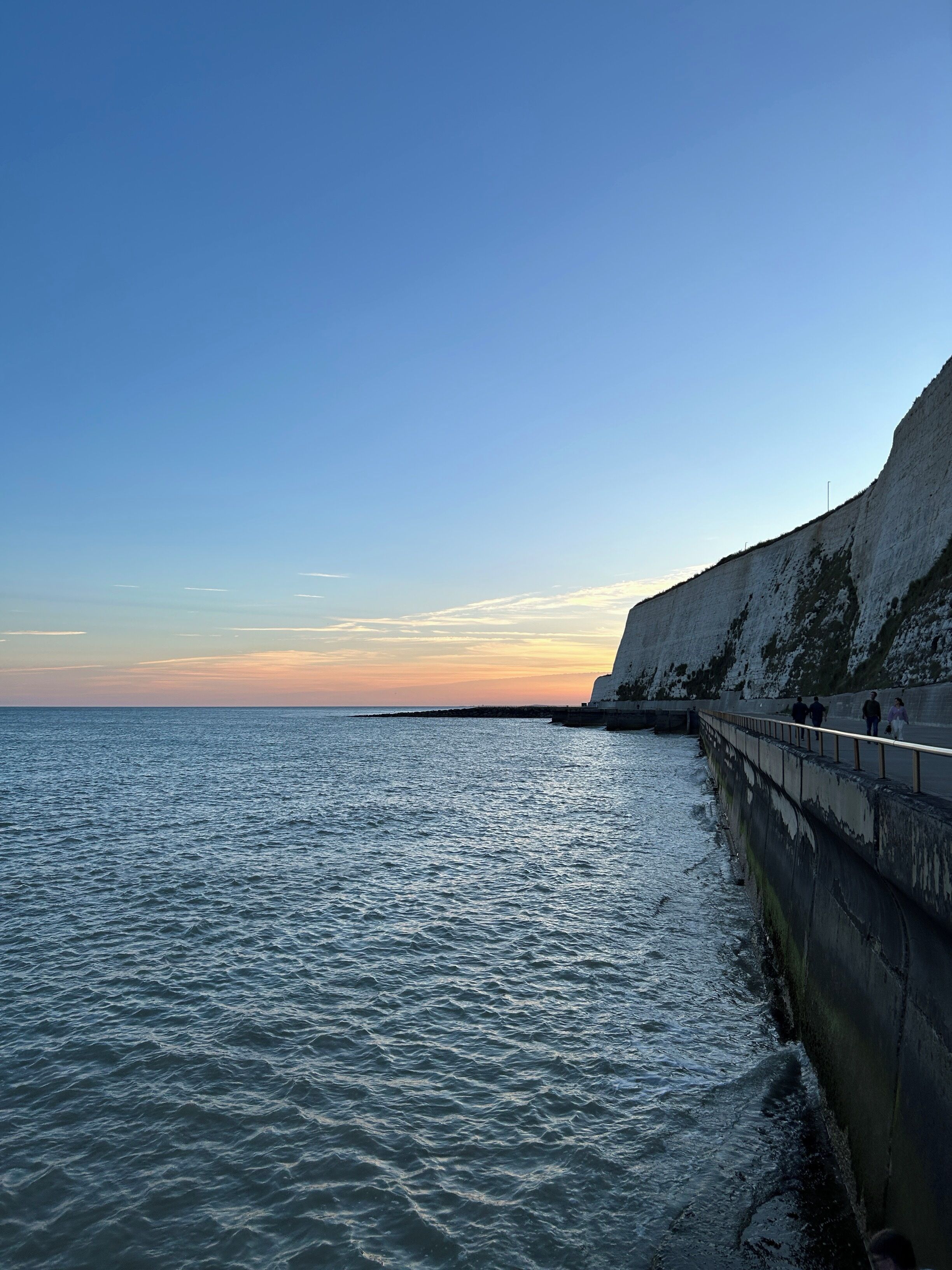 A coastal scene with a concrete sea wall and a clear sky.