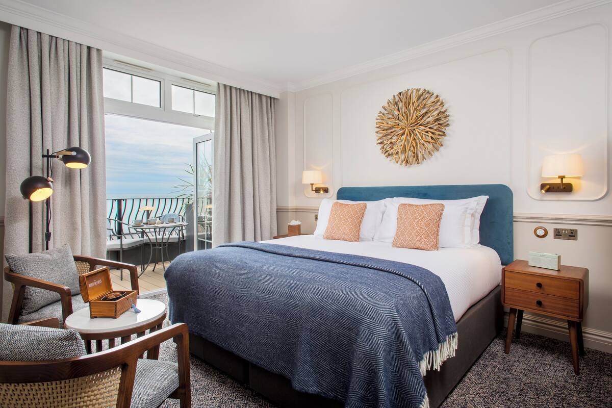 A hotel room with a large bed, a chair, a small table, and a view of the outdoors.