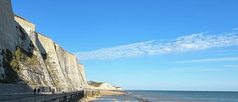 A coastal walkway with a steep cliff on one side and a beach on the other.