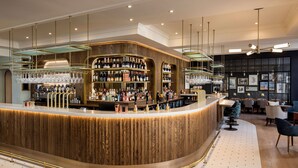 A modern bar area with a curved counter, multiple shelves of bottles, and a seating area with chairs and tables. - White Horses by Everly Hotels Collection (Brighton)