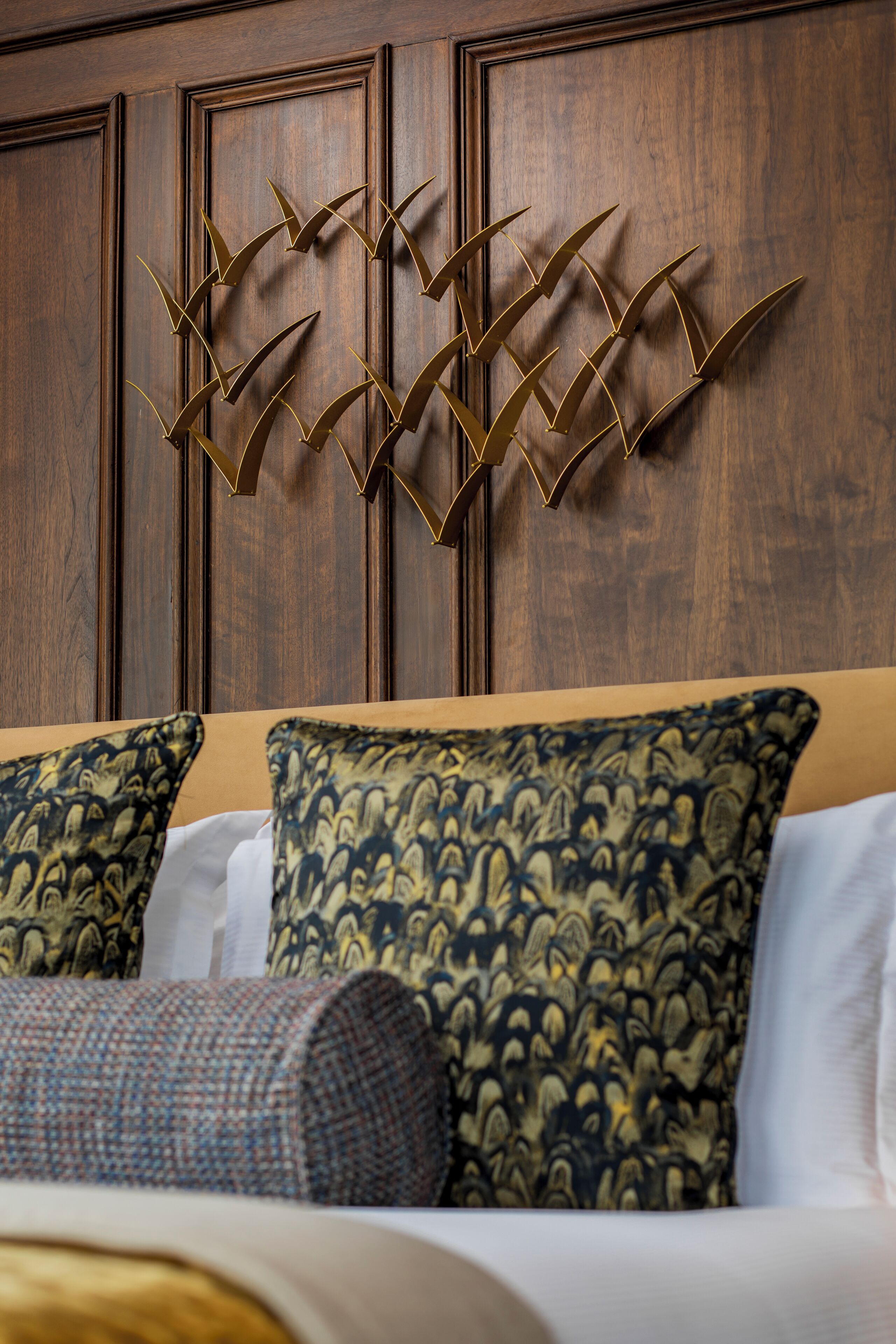 A bedroom with a wooden headboard, patterned pillows, and a decorative wall piece.