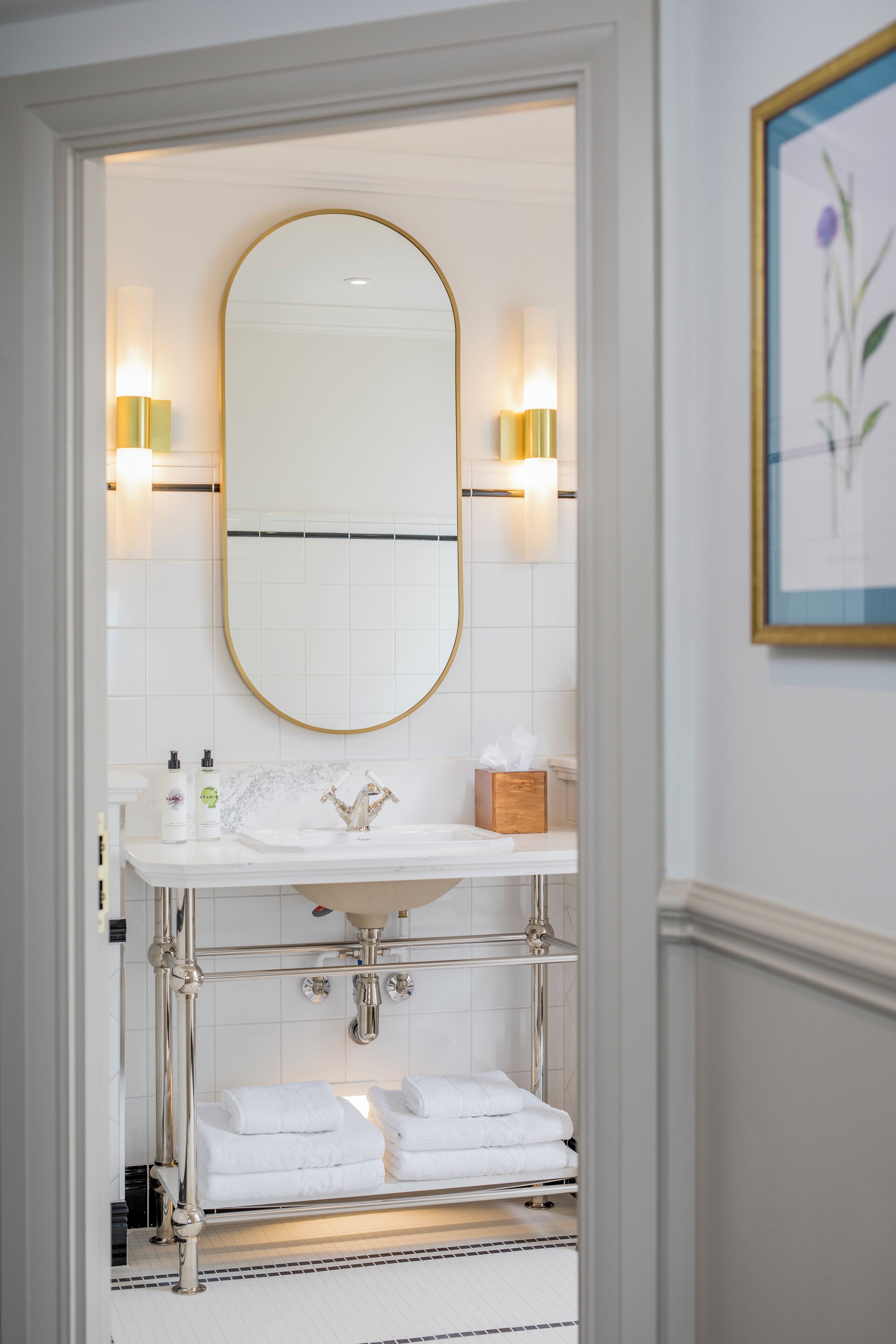 A bathroom with a white vanity, a gold-framed mirror, and two wall-mounted lights.