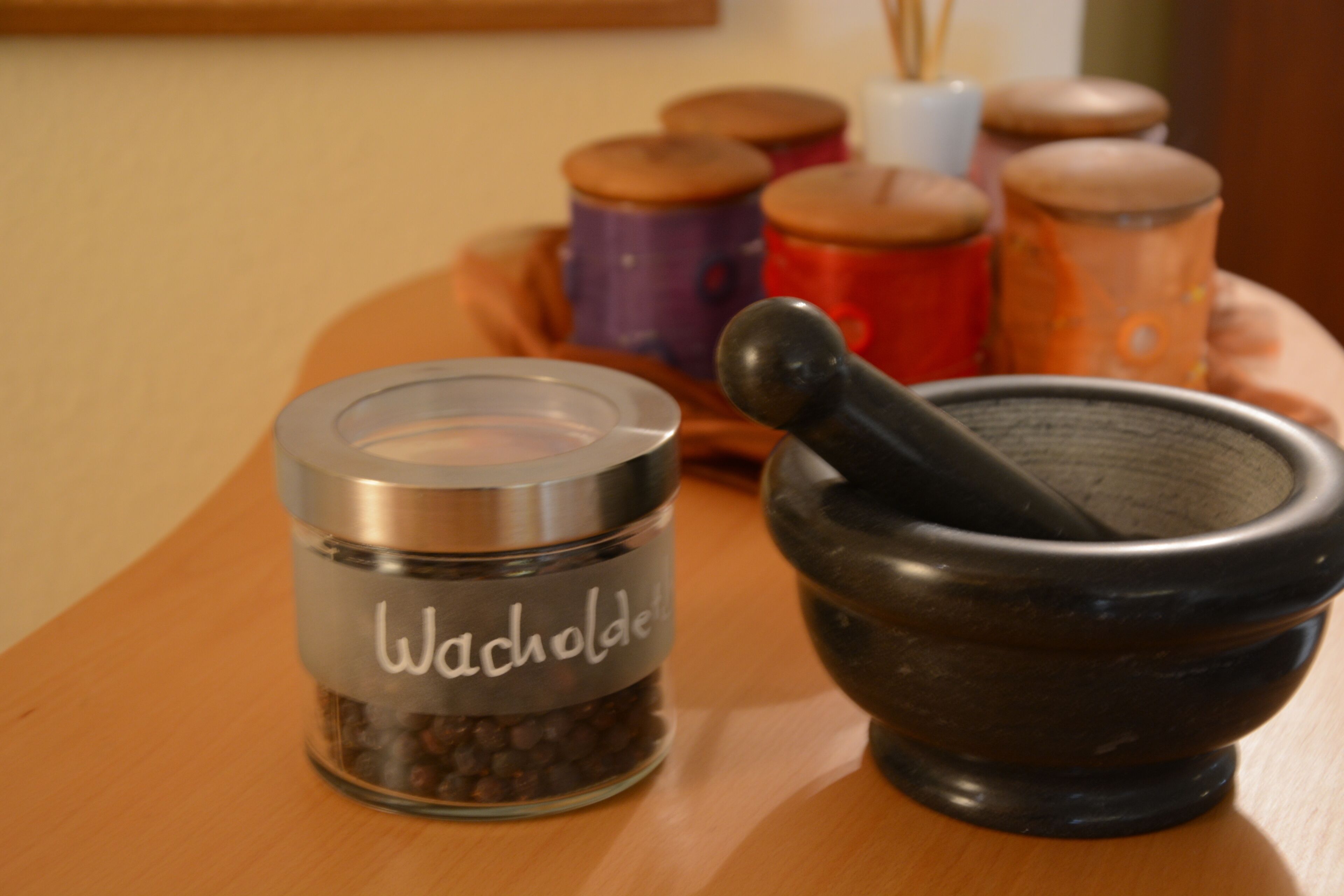 A wooden table with a spice jar labeled "Wacholder" and a mortar and pestle.