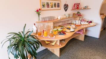 A buffet setup with various food items and drinks, a potted plant, and a framed picture on the wall.