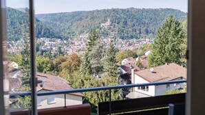A view from a balcony overlooking a town nestled in a valley with dense forests and a hill with a tower. - Aparthotel Hochwald (Bad Liebenzell)