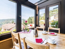 Un comedor con una mesa dispuesta para dos personas, amplias ventanas que ofrecen vistas a un paisaje montañoso.
