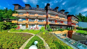 A multi-story hotel with balconies, a garden area with seating, and a clear sky. - Aparthotel Hochwald (Bad Liebenzell)