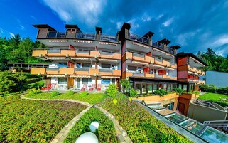 Un hotel de varios pisos con balcones, un jardín con asientos y un cielo despejado.