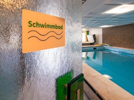 Letrero que dice 'Schwimmbad' en una pared texturizada, indicando la zona de la piscina.