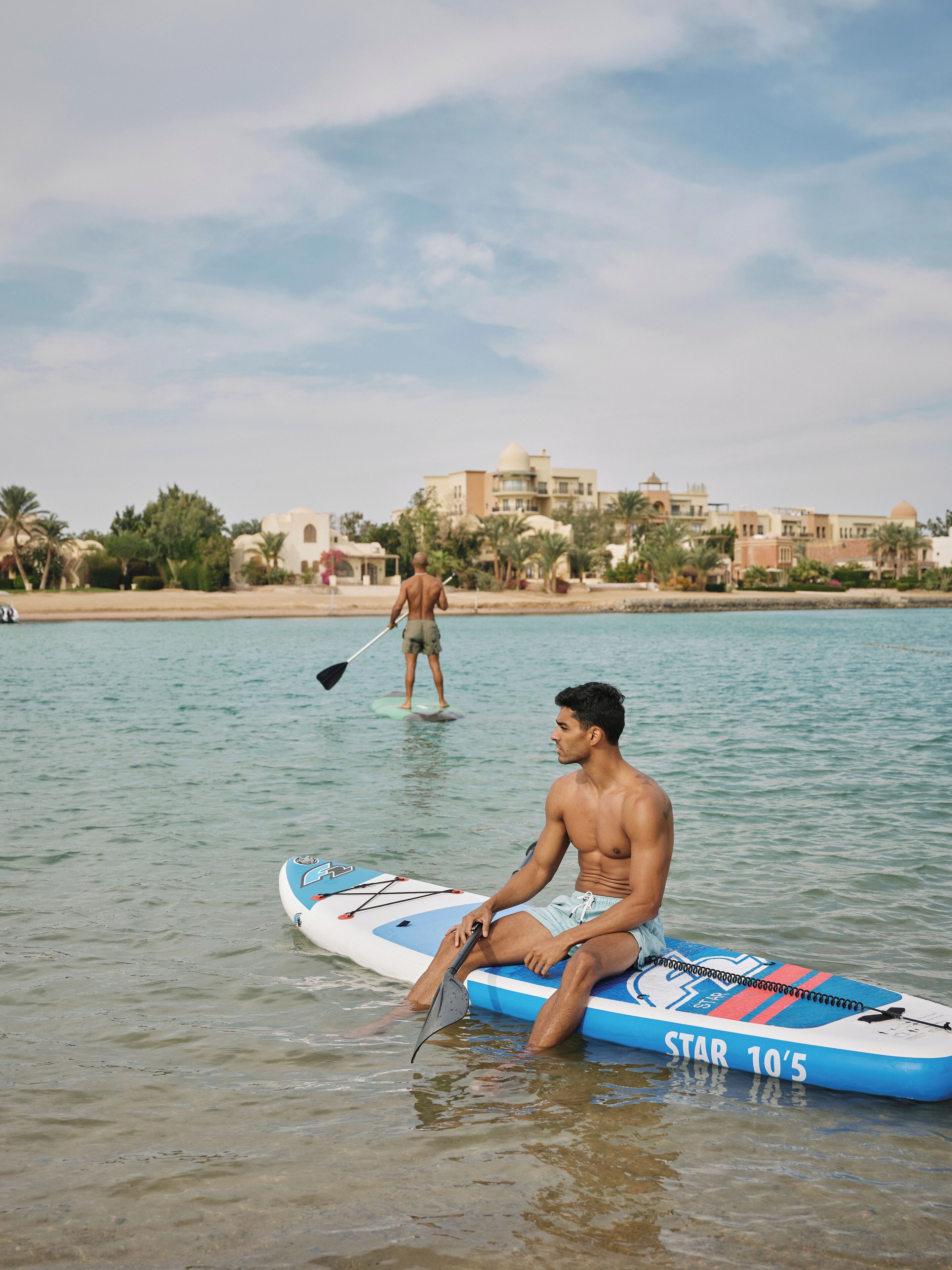 Un homme est assis sur une planche à pagaie, sur des eaux calmes, avec une vue sur la ville en arrière-plan.